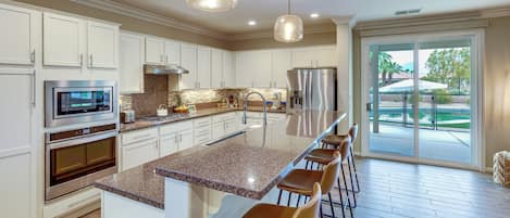 A modern kitchen with white cabinets, stainless steel appliances, a granite countertop, and a bar area with stools.