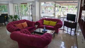 Uma sala de estar ampla com dois sofás vermelhos confortáveis, uma mesa de centro e uma televisão sobre um suporte.