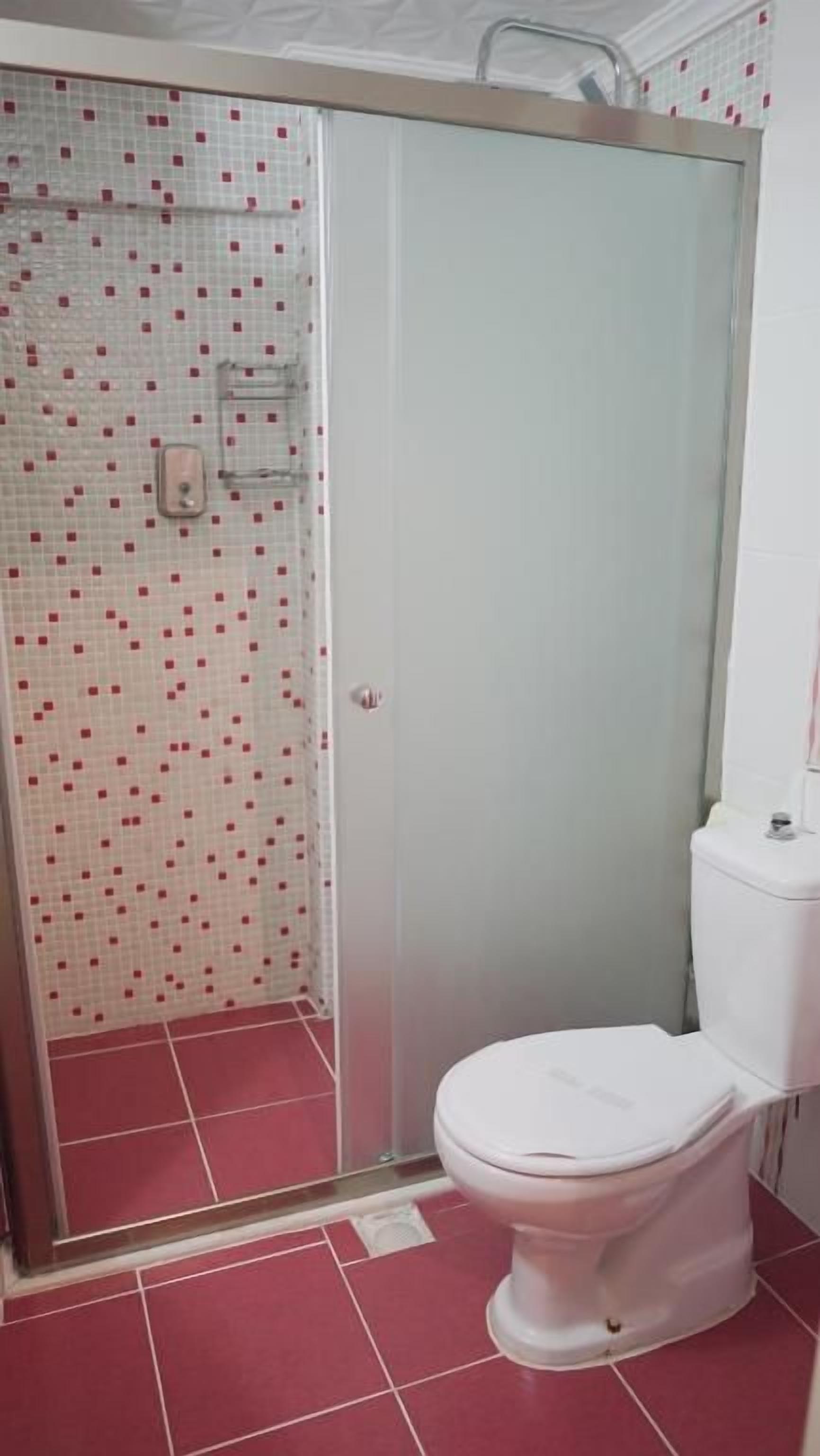 Un baño con ducha de vidrio, inodoro blanco y piso de baldosas.