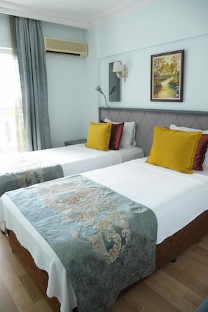 Habitación de hotel con dos camas, un ventanal con cortinas, un cuadro en la pared y una mesita de noche con lámpara.