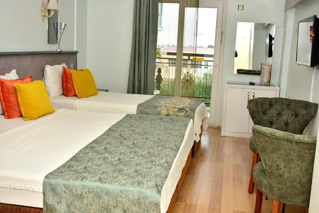 Habitación de hotel con dos camas, una silla verde, un escritorio pequeño y un balcón con vistas.