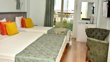 Habitación de hotel con dos camas, una silla verde, un escritorio pequeño y un balcón con vistas.
