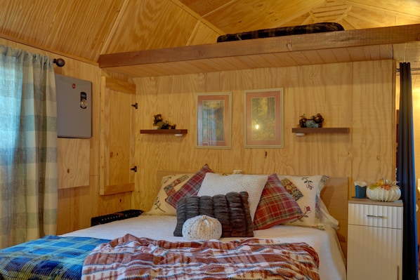Een houten interieur met een bed, kussens, een deken, een thermostaat en ingekaderde foto's aan de muur.