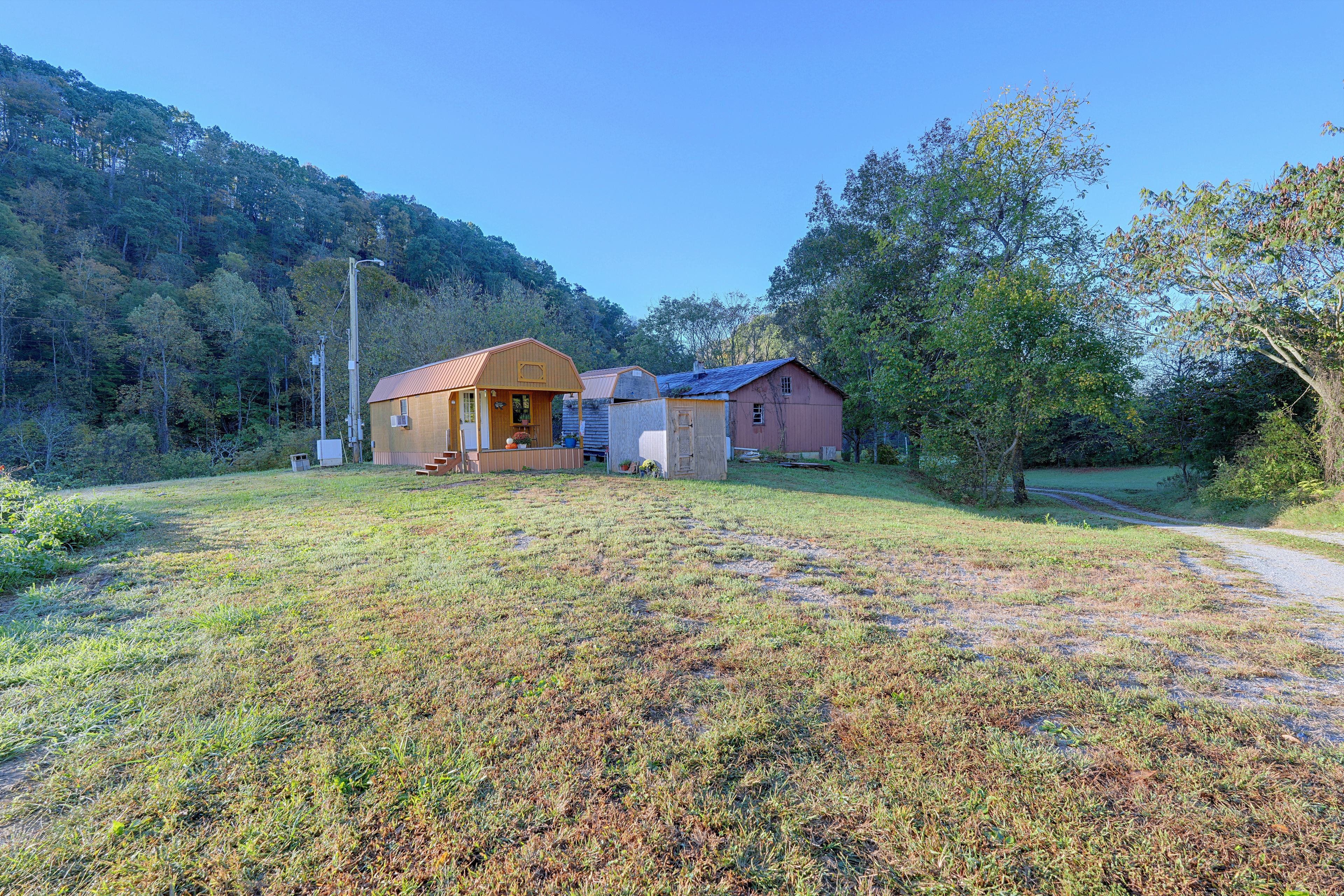 Una propietat rural amb una casa principal, un cobert més petit i una granja. Hi ha un camp de gespa al davant, un camí de terra a la dreta i un turó amb arbres al fons.