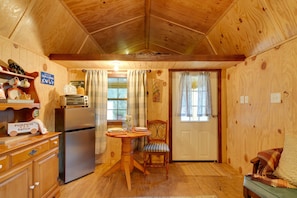 Een houten interieur met een keukenhoek, inclusief een koelkast, een eettafel met stoelen en een raam met gordijnen.