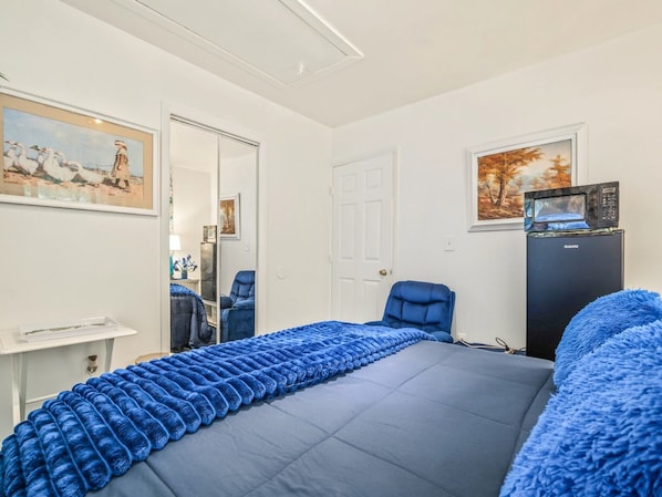 Un dormitorio con cama, escritorio, silla y refrigerador.