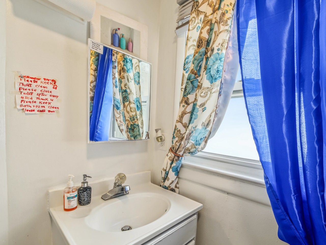 A bathroom with a sink, mirror, and a note on the wall.