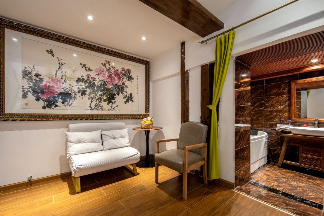 A room with a sofa, a chair, a small table with a basket, a large framed artwork on the wall, and a bathroom with a marble floor and wooden vanity.