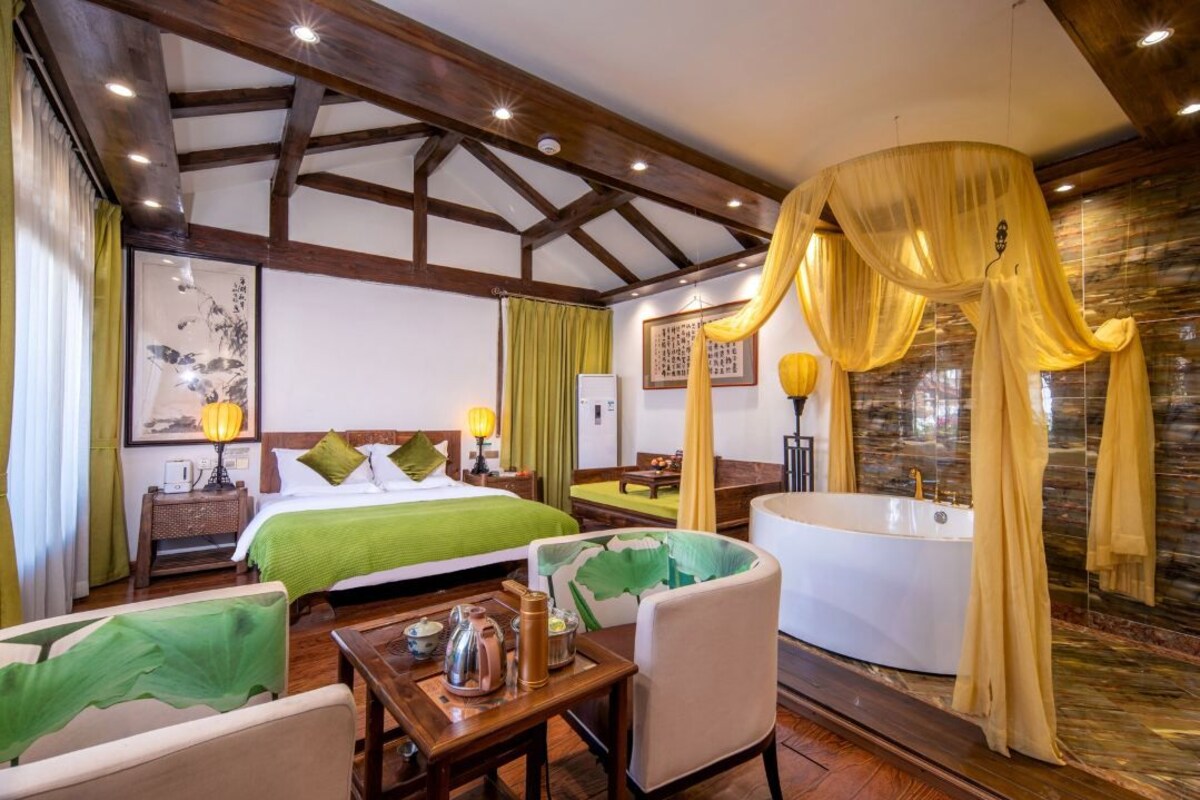 A hotel room with a large bed, a sitting area, a bathtub, and a dining table.