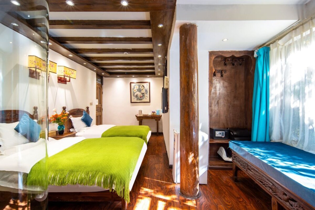 A hotel room with two beds, a wooden floor, a large pillar, a shower area, and a painting on the wall.
