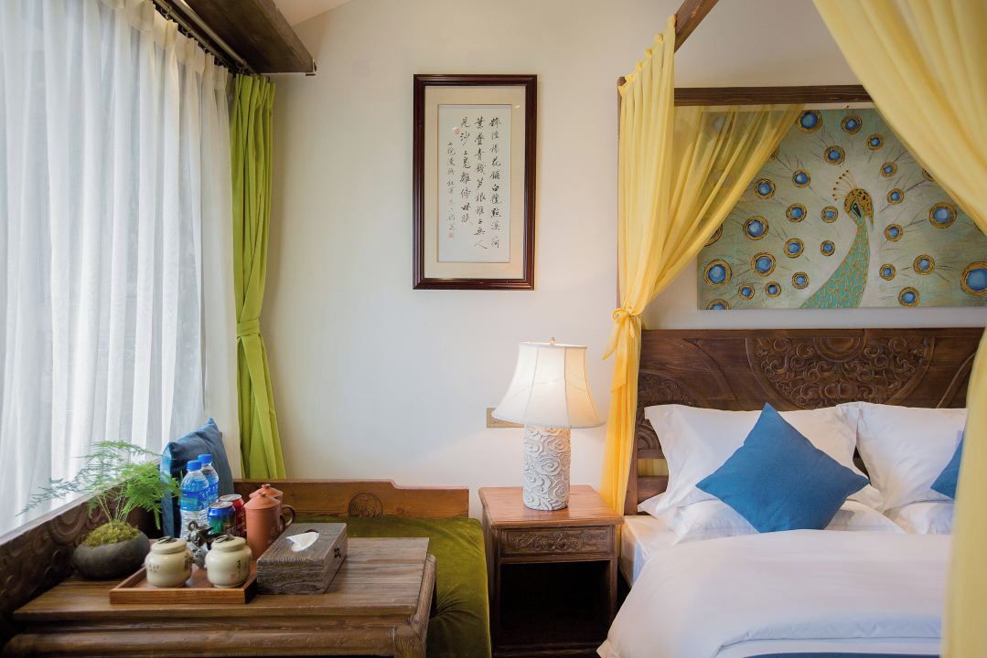 A hotel room with a bed, bedside table, lamp, and a wall with a framed picture.