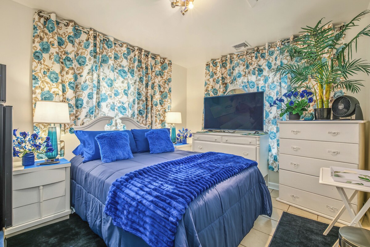 A bedroom with a bed, a television, a dresser, and a potted plant.