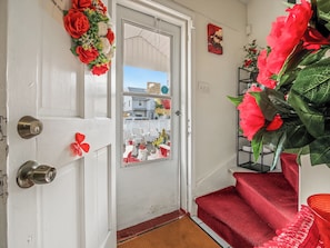 A white door with a red doormat, a red carpeted staircase, and a shelf with red flowers. - Private Room&Bath in Owner-Occupied Home (Bridgeport)