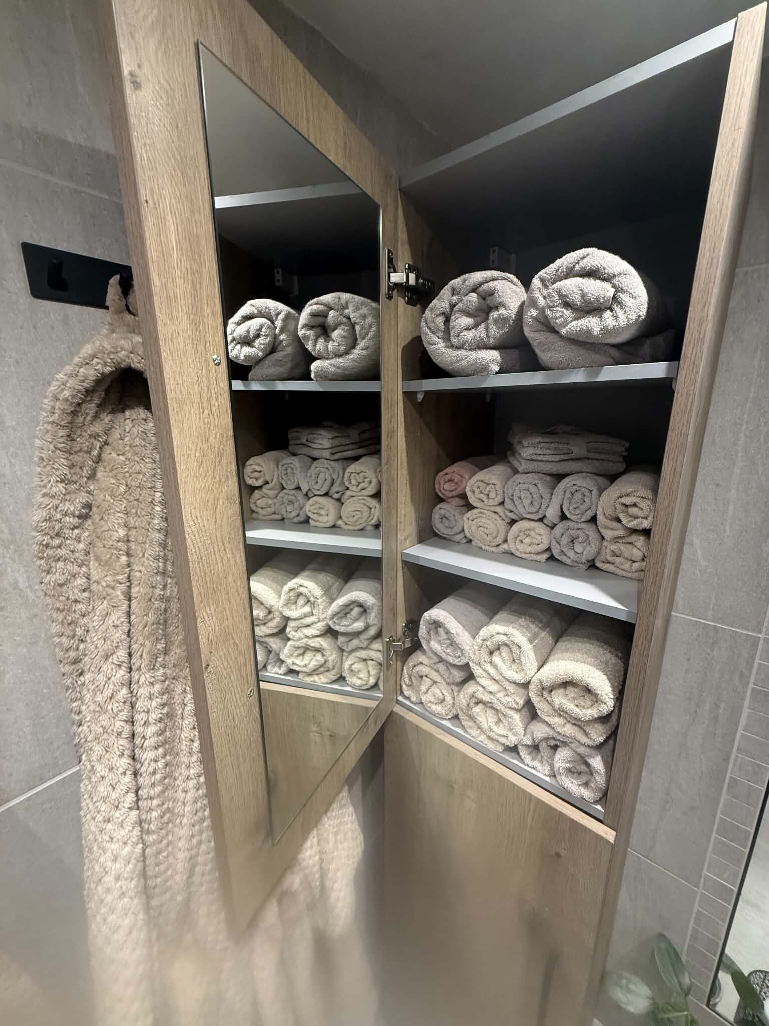 A wooden cabinet with multiple shelves holding rolled towels.