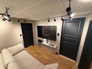Una sala de estar moderna con una televisión de pantalla plana montada en la pared, un sofá y un ventilador de techo.