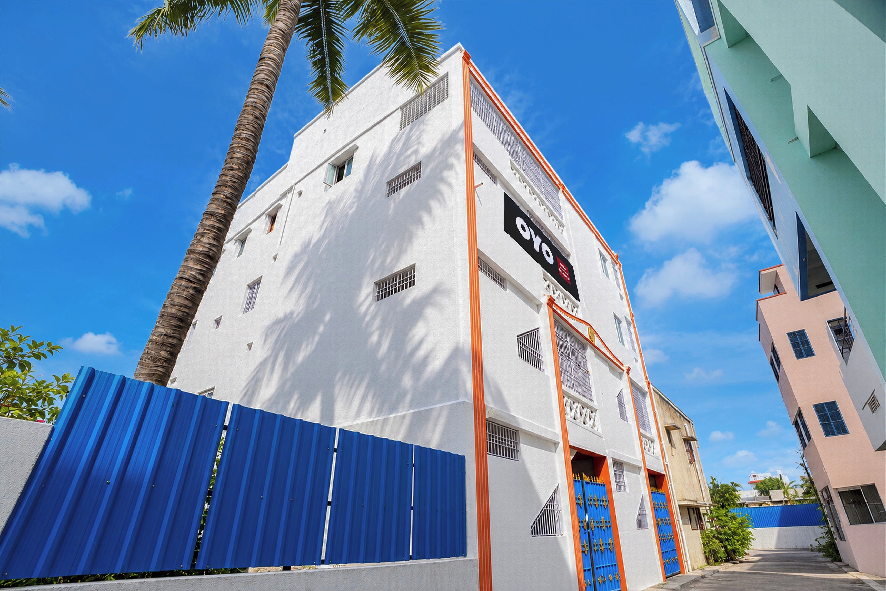 Un edificio blanco con una puerta azul, un letrero con el logotipo 'OYO' y una palmera.