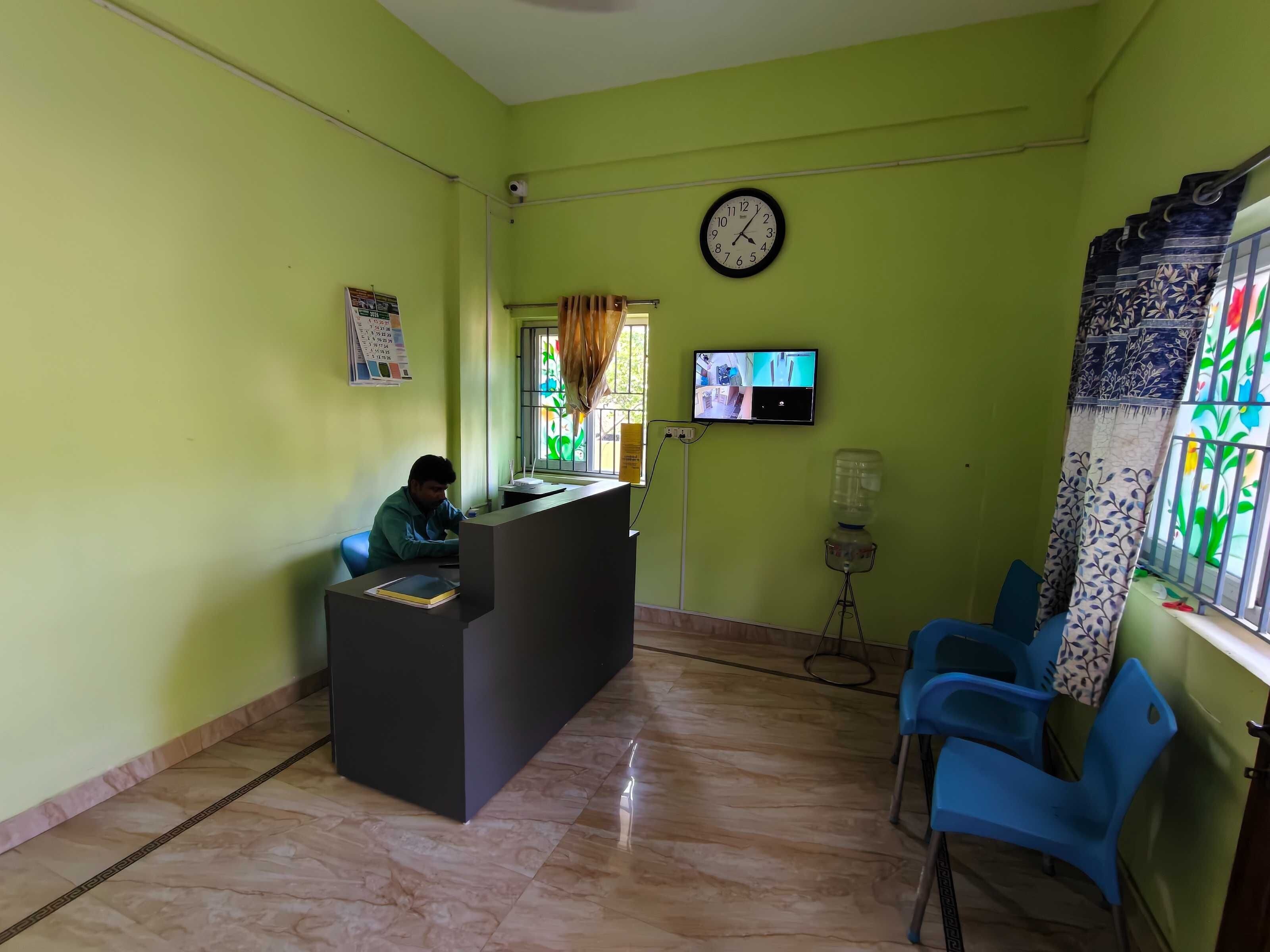 Un área de recepción con mostrador, sillas, un reloj, un televisor y dispensador de agua.