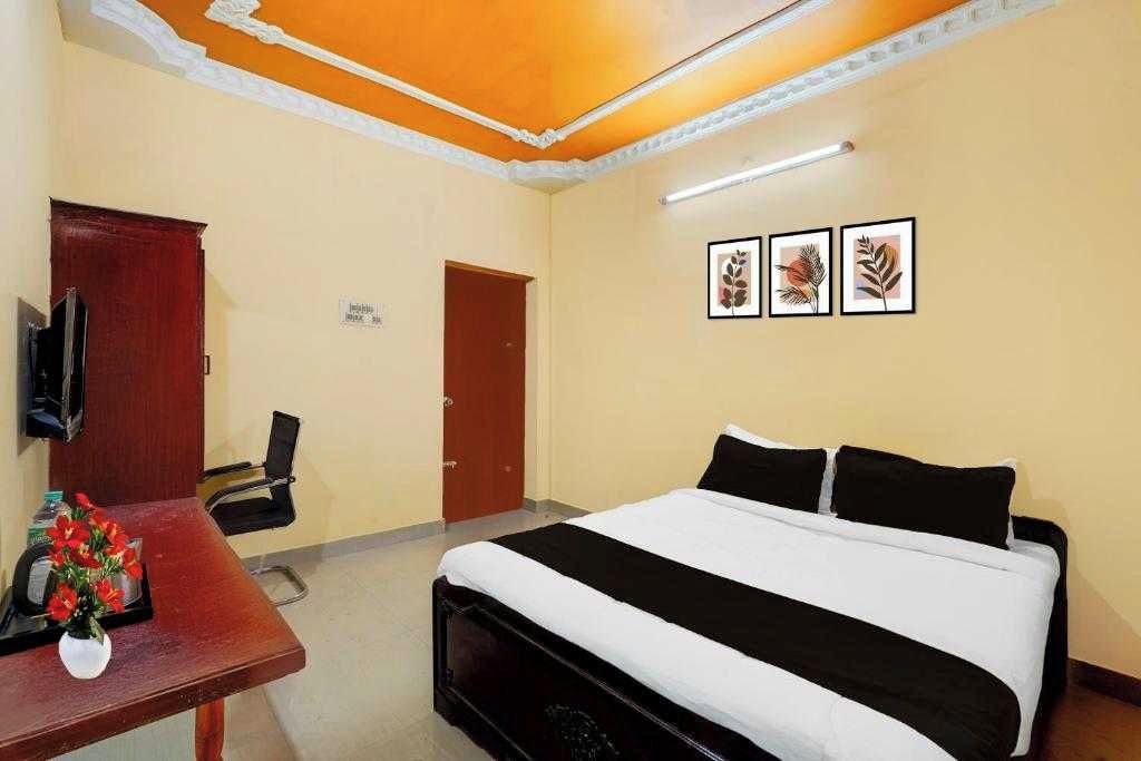 Habitación de hotel con cama, escritorio con un jarrón de flores, televisión y cuadros en la pared.