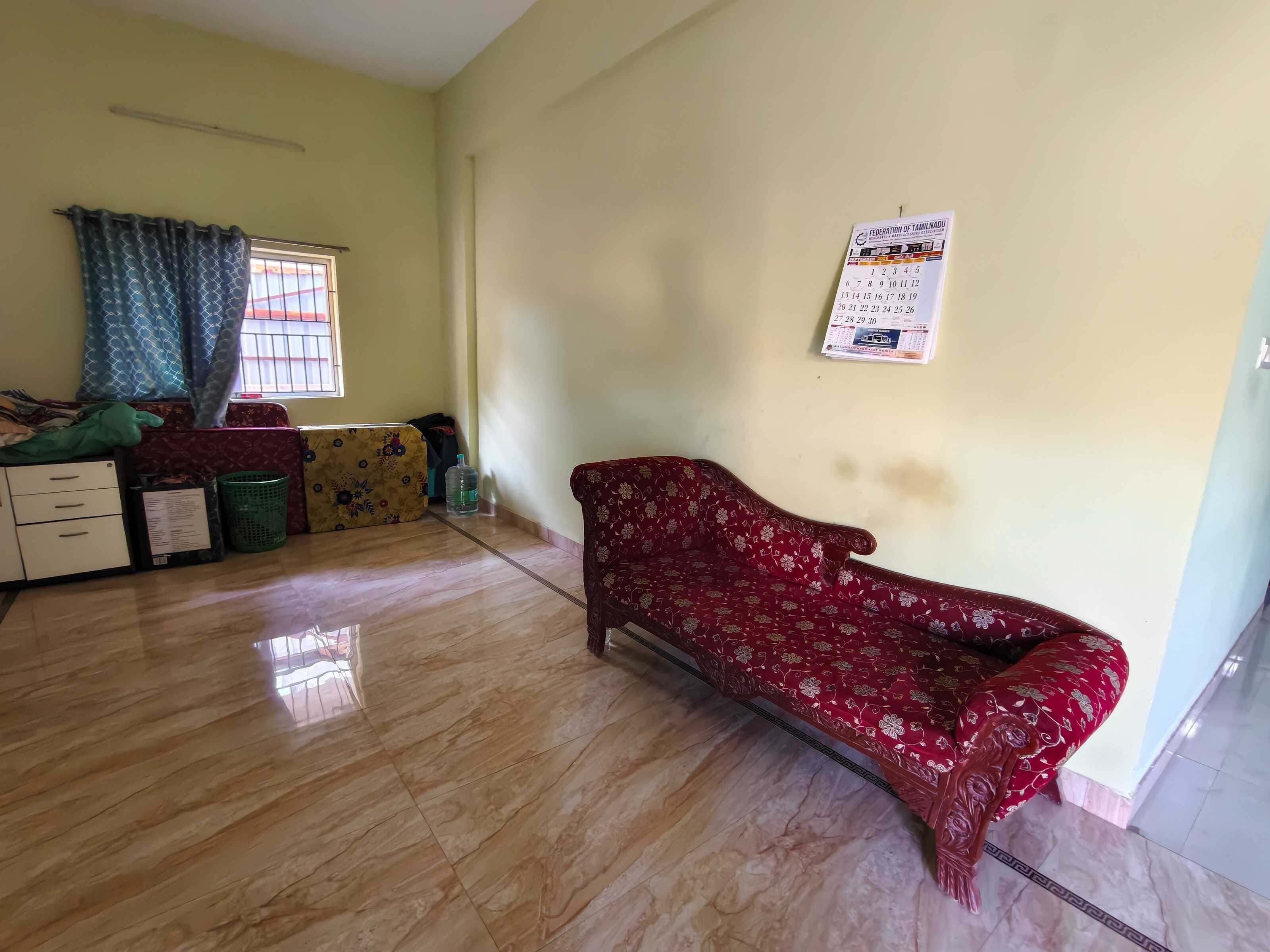 Una habitación con sofá, cama, ventana con cortinas, un calendario en la pared y un dispensador de agua.