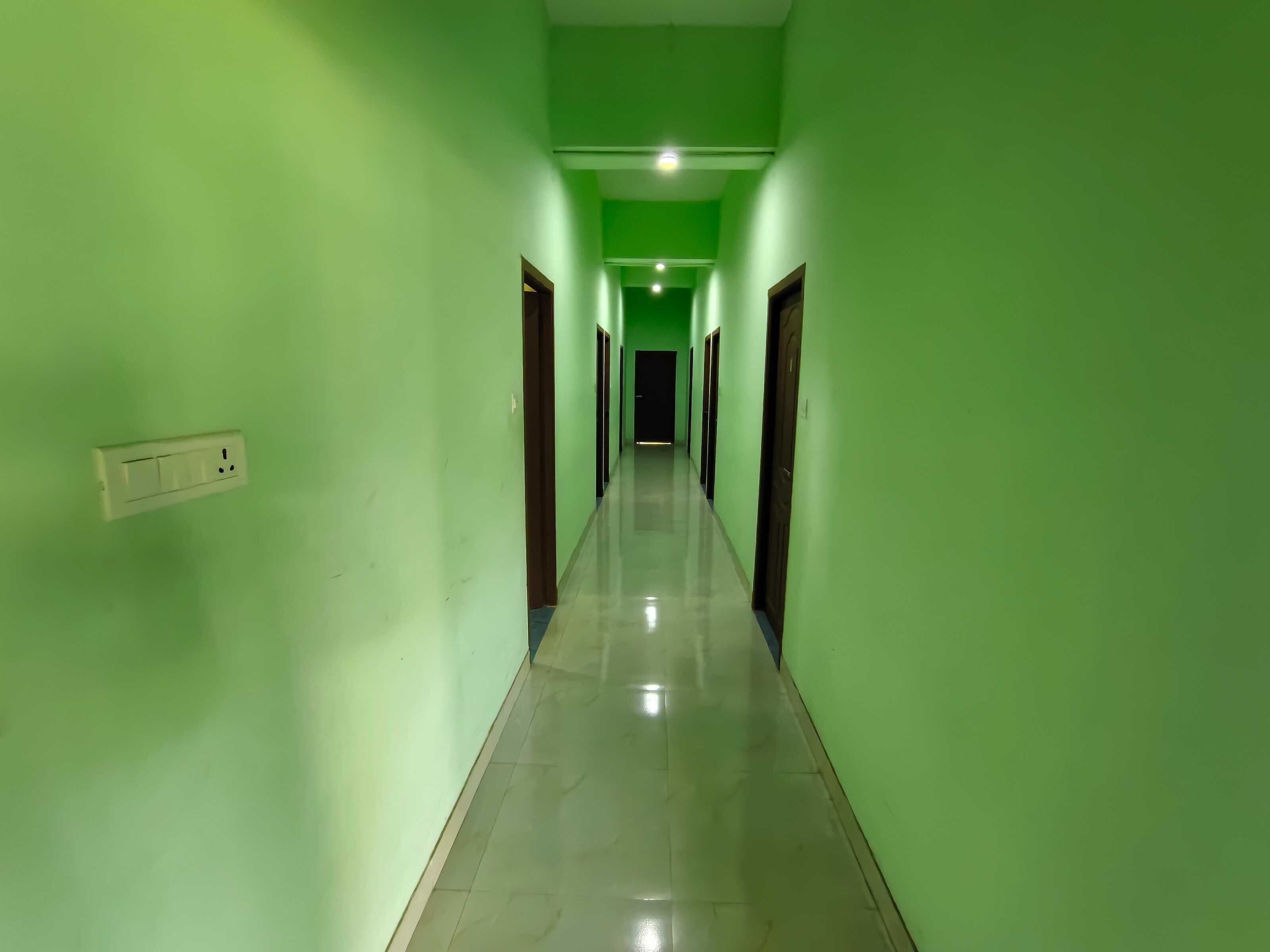 Un pasillo con paredes verdes y piso de baldosas, que conduce a una puerta al final.