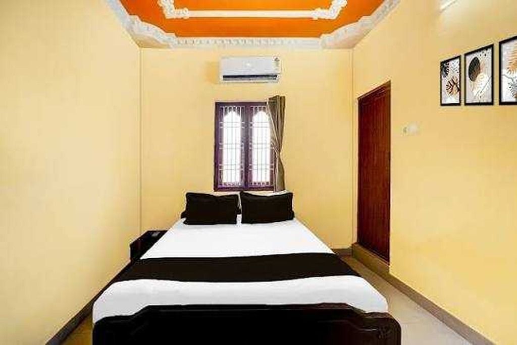 Habitación de hotel con cama, unidad de aire acondicionado, ventana con cortinas y una obra de arte enmarcada en la pared.