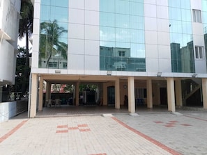 Un edificio moderno con fachada de vidrio, un área de entrada cubierta y un suelo pavimentado con marcas rojas.
