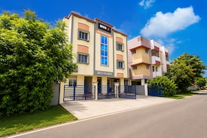 A multi-story hotel with a prominent 'OYO' sign, a gated entrance, and a well-maintained lawn. - Hotel O NL Residency (Chengalpattu)