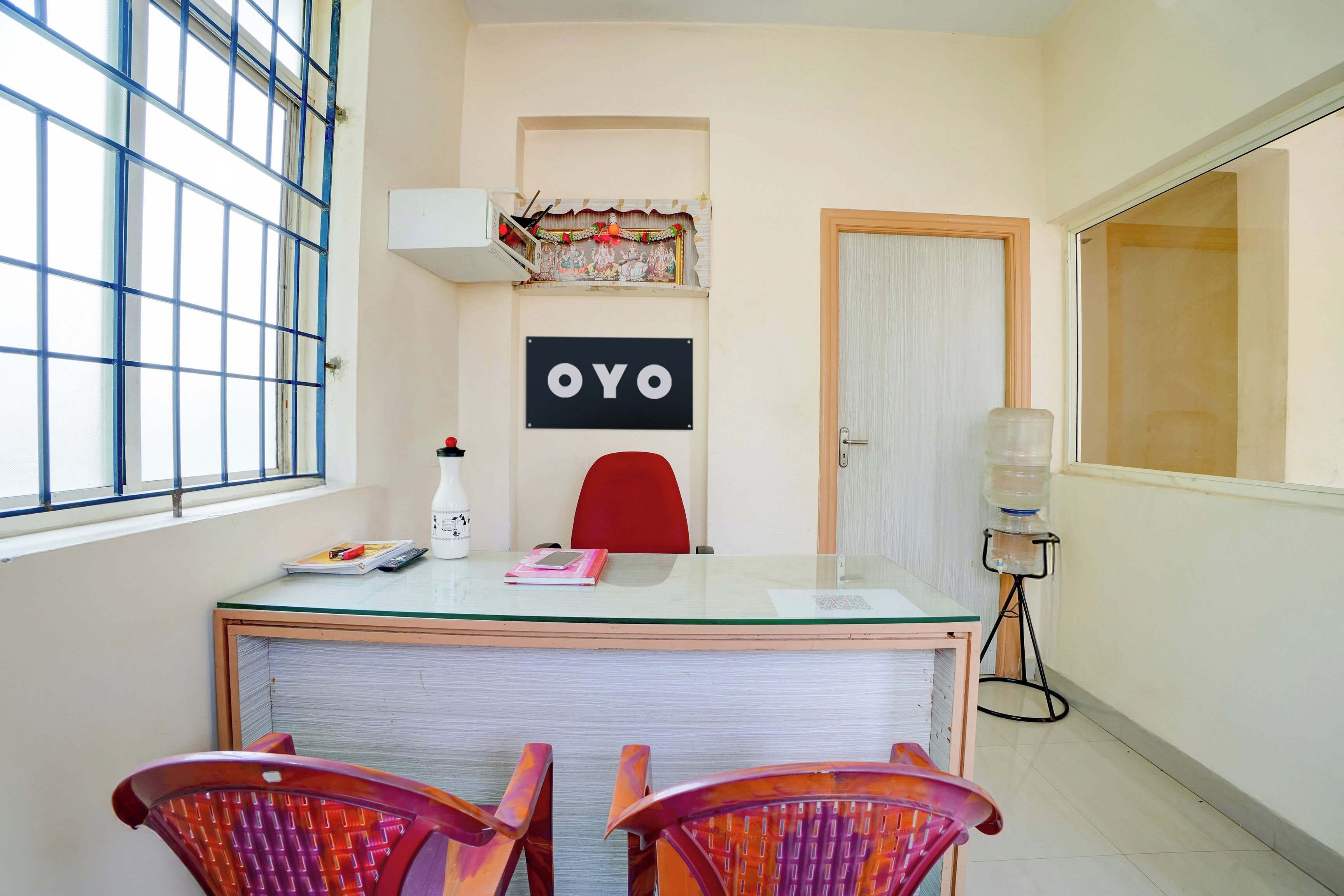 Een kamer met een glazen bureau, twee stoelen, een waterdispenser, een deur en een bord aan de muur.