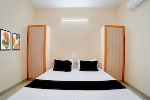 Une chambre d’hôtel avec un lit, deux oreillers noirs, un couvre-lit blanc, un plaid noir, deux œuvres d’art encadrées accrochées au mur et un luminaire au plafond.