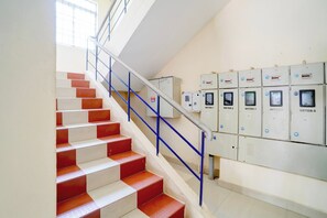 A staircase with red and white steps, blue handrails, and a row of electrical meters on the wall. - Hotel O NL Residency (Chengalpattu)