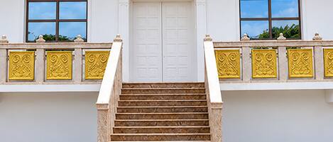 Una escalera conduce a una puerta blanca con barandilla de balcón que presenta detalles dorados decorativos.