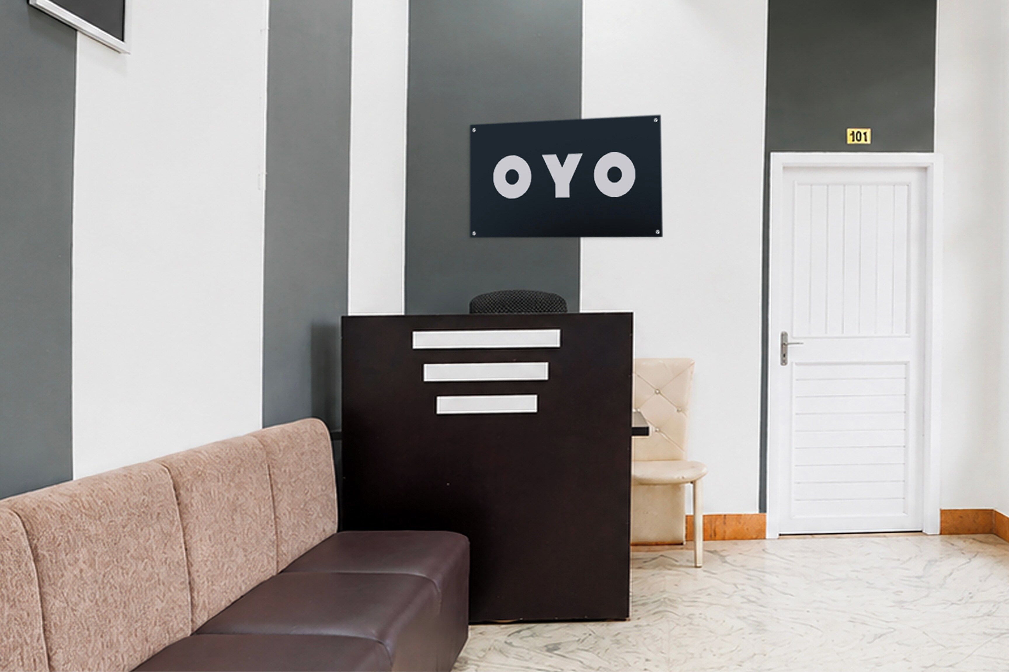 A reception area with a black sign reading 'OYO' above a desk, a beige sofa, and a white door in the background.