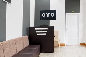 Un área de recepción con un letrero negro que dice 'OYO' sobre un mostrador, un sofá color beige y una puerta blanca al fondo.