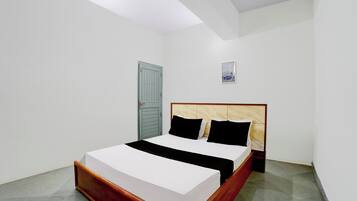 Una cama individual con estructura de madera y ropa de cama blanca en una habitación con paredes blancas y suelo gris.