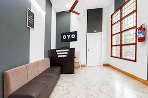 Un área de recepción con un sofá marrón, un mostrador negro, un ventilador de techo, una puerta con un letrero de número y un extintor.