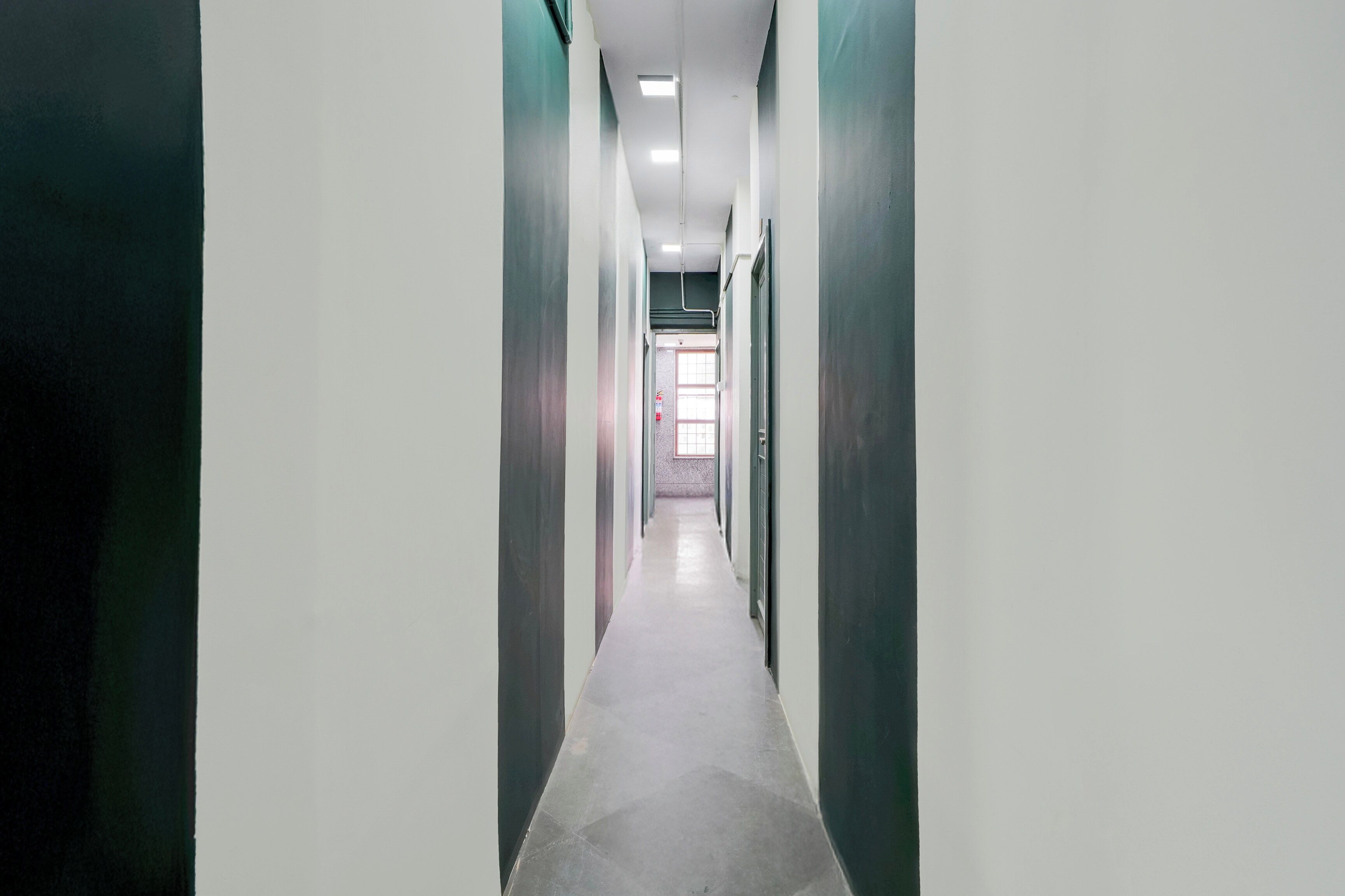 Un pasillo largo y estrecho con puertas a ambos lados, que conduce a una habitación al final de la cual hay una ventana.