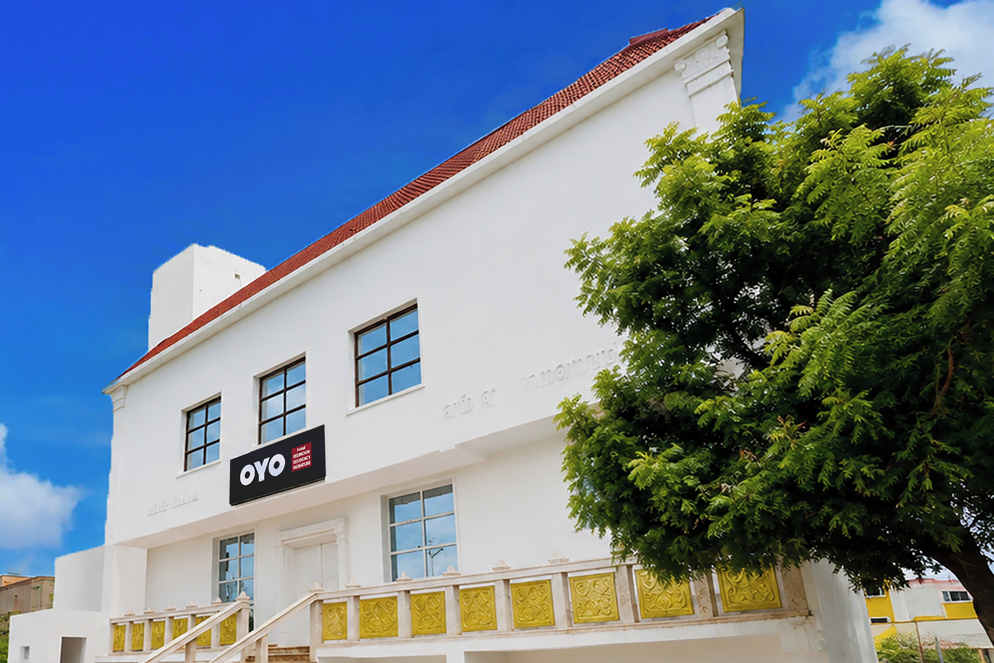 Un edificio blanco con techo rojo, un letrero que dice 'OYO Hotel Residencia Signature' y una escalera que lleva a la entrada.