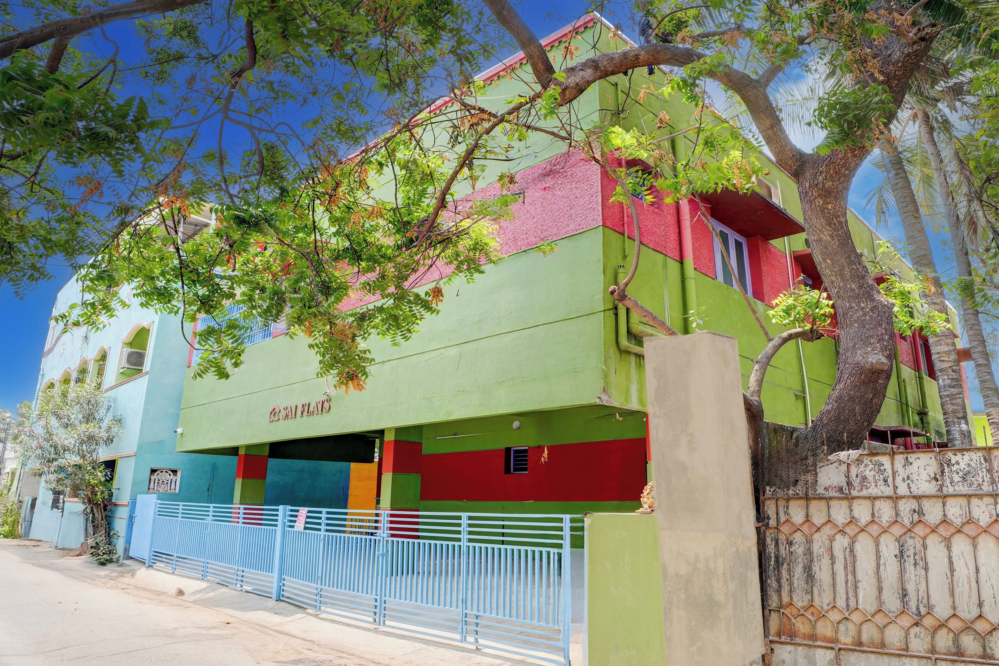 Un edificio de varios pisos con fachada verde y un cartel que dice 'SAI FLATS'.