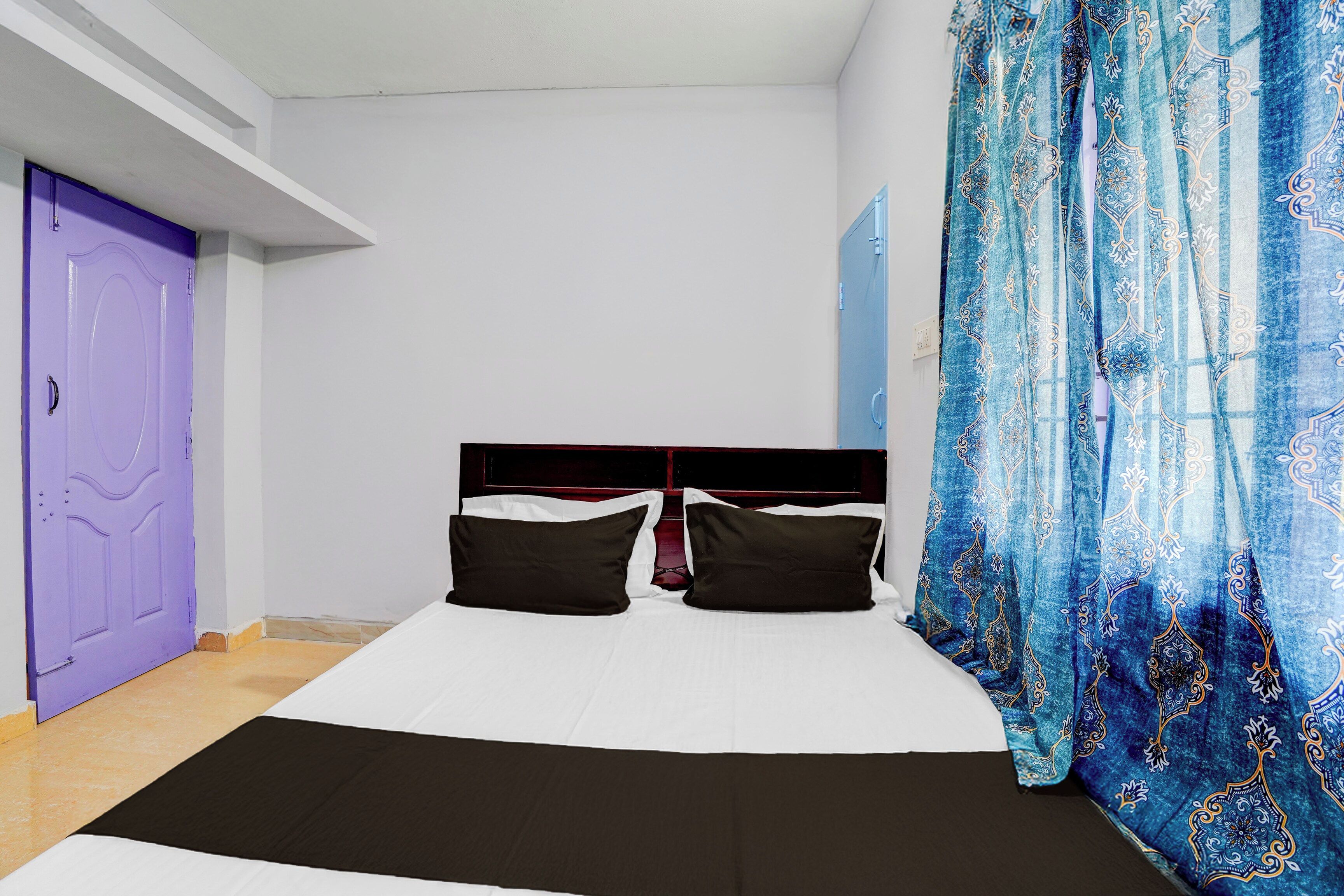 Ein Zimmer mit einem Bett, einer violetten Tür und einem blauen, gemusterten Vorhang.