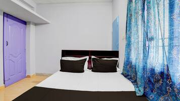 Ein Zimmer mit einem Bett, einer violetten Tür und einem blauen, gemusterten Vorhang.