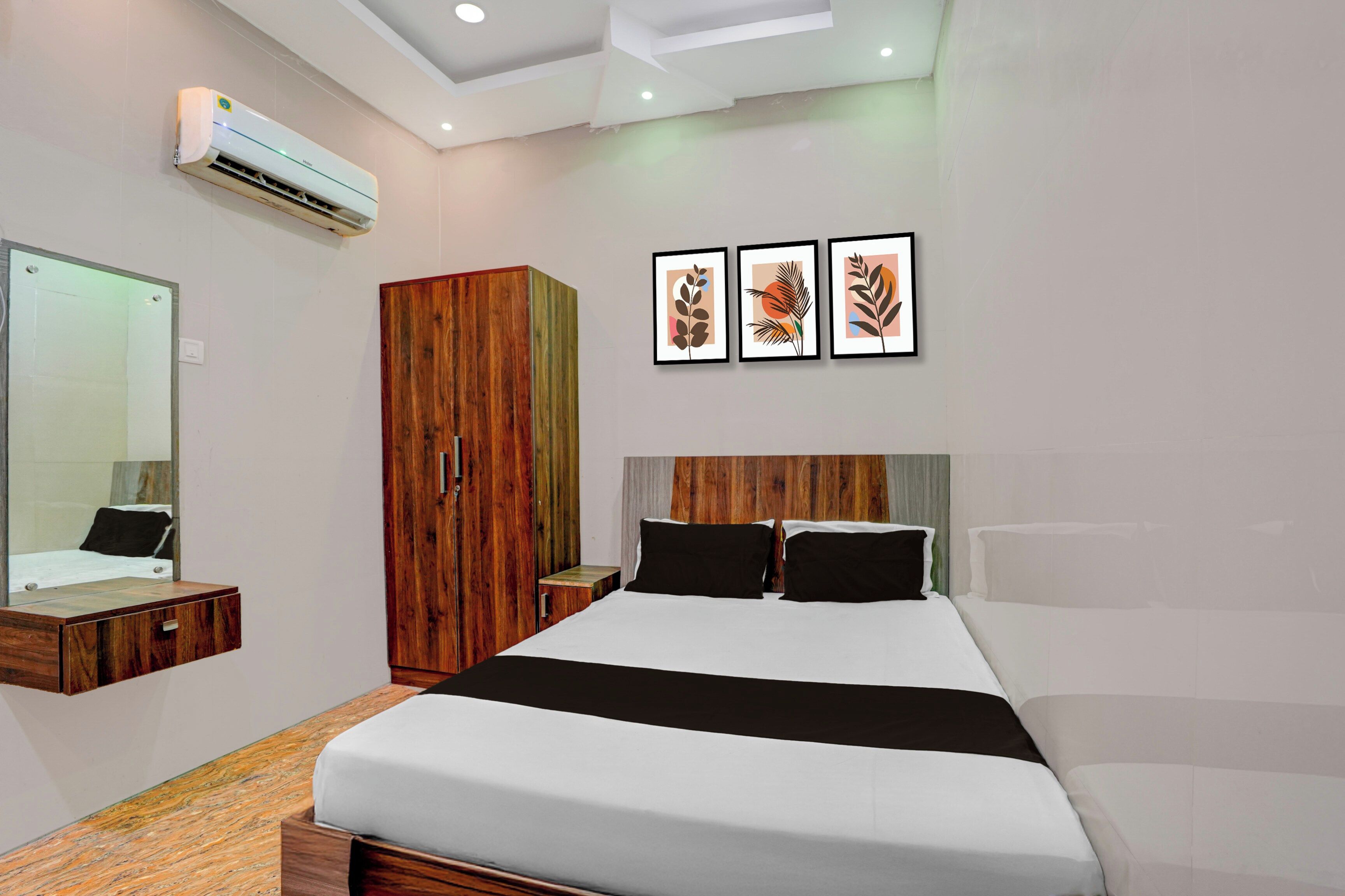 A modern bedroom with a large bed, a wardrobe, a mirror, and three framed artworks on the wall.
