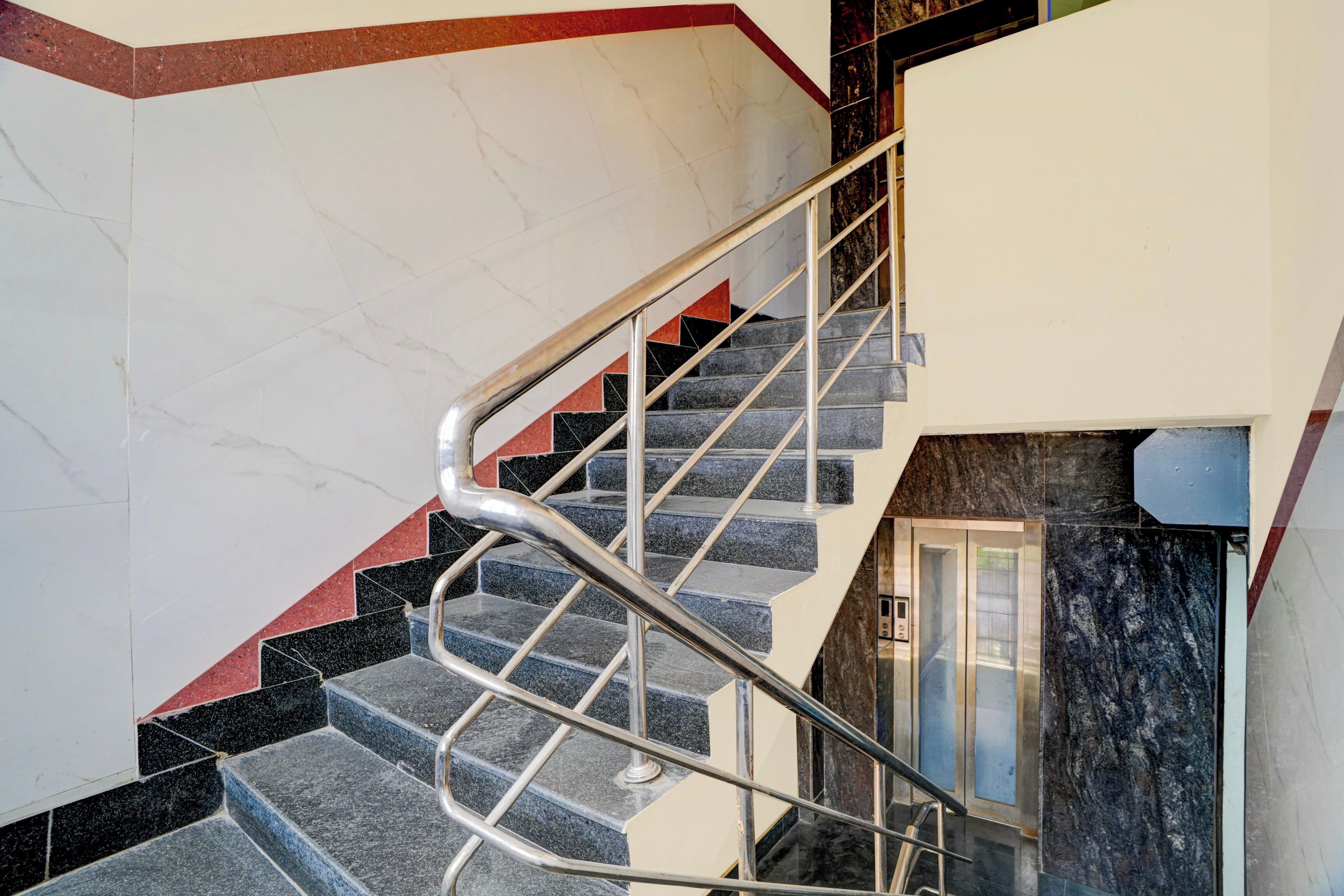 A staircase with a metal handrail, marble walls, and a corner with a red accent.