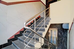 Una escalera con barandilla de metal, paredes de mármol y un rincón con detalles en rojo.