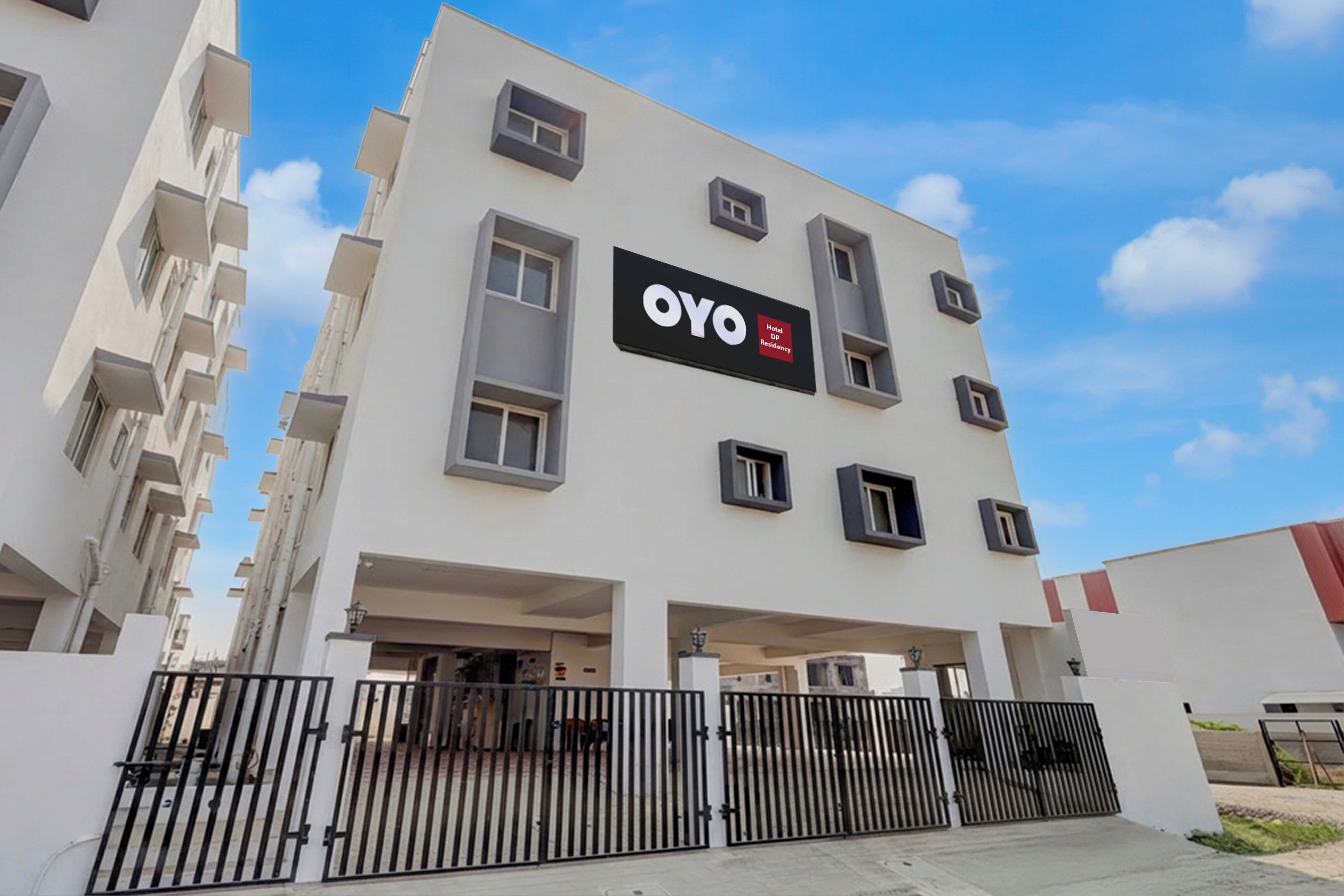 A modern hotel building with a prominent 'OYO' sign, multiple balconies, and a gated entrance.