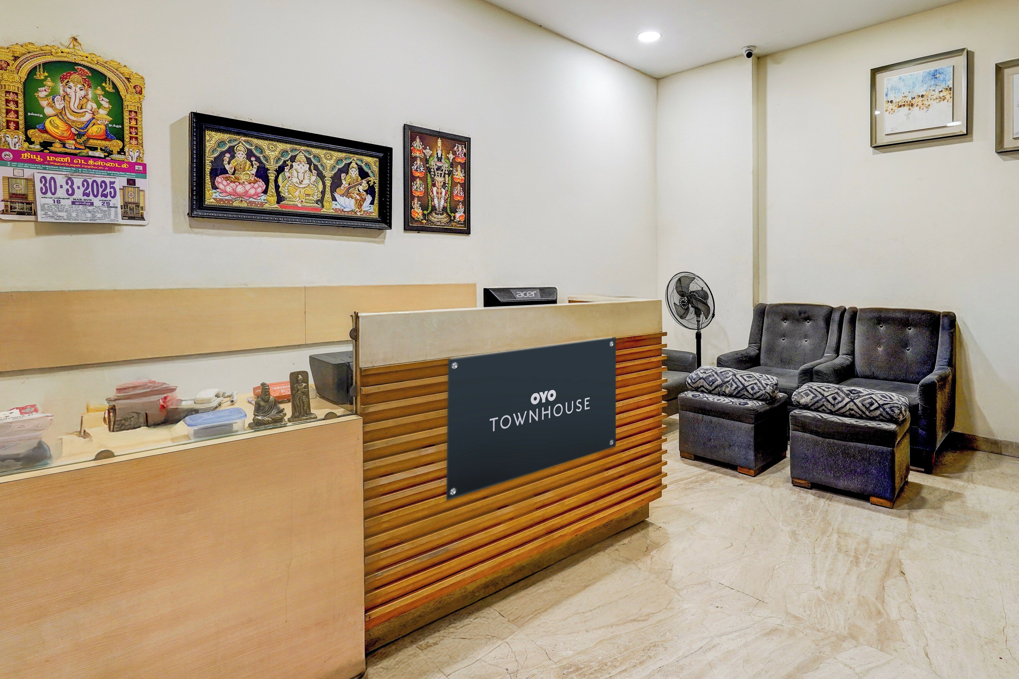 A reception area with a wooden counter, a sign reading 'OYO TOWNHOUSE,' and a seating area with two chairs.