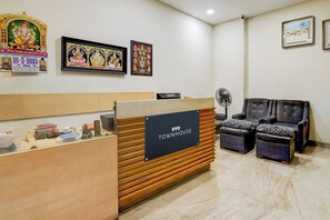 A reception area with a wooden counter, a sign reading 'OYO TOWNHOUSE,' and a seating area with two chairs.