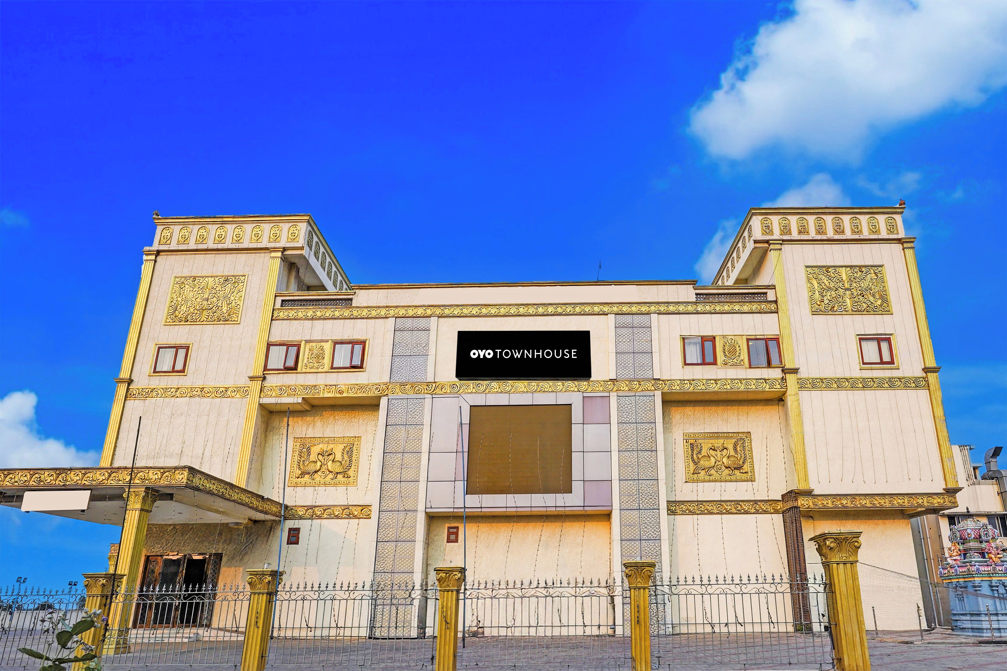 Un bâtiment orné de décorations dorées, doté d’une entrée centrale et d’une enseigne indiquant « OYO TOWNHOUSE ».