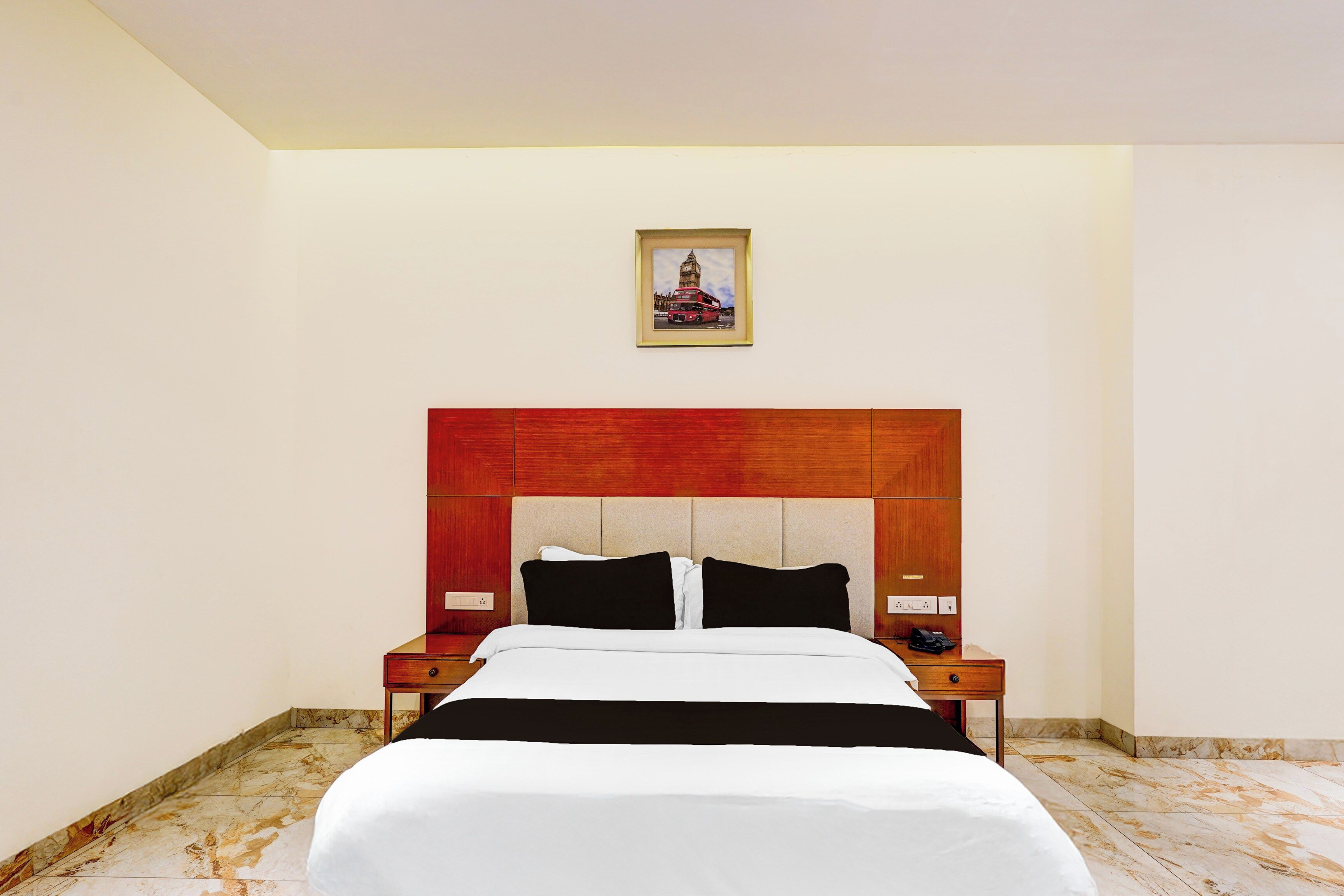 Une chambre d’hôtel avec un lit, une table de chevet, un tableau accroché au mur et un sol en marbre.