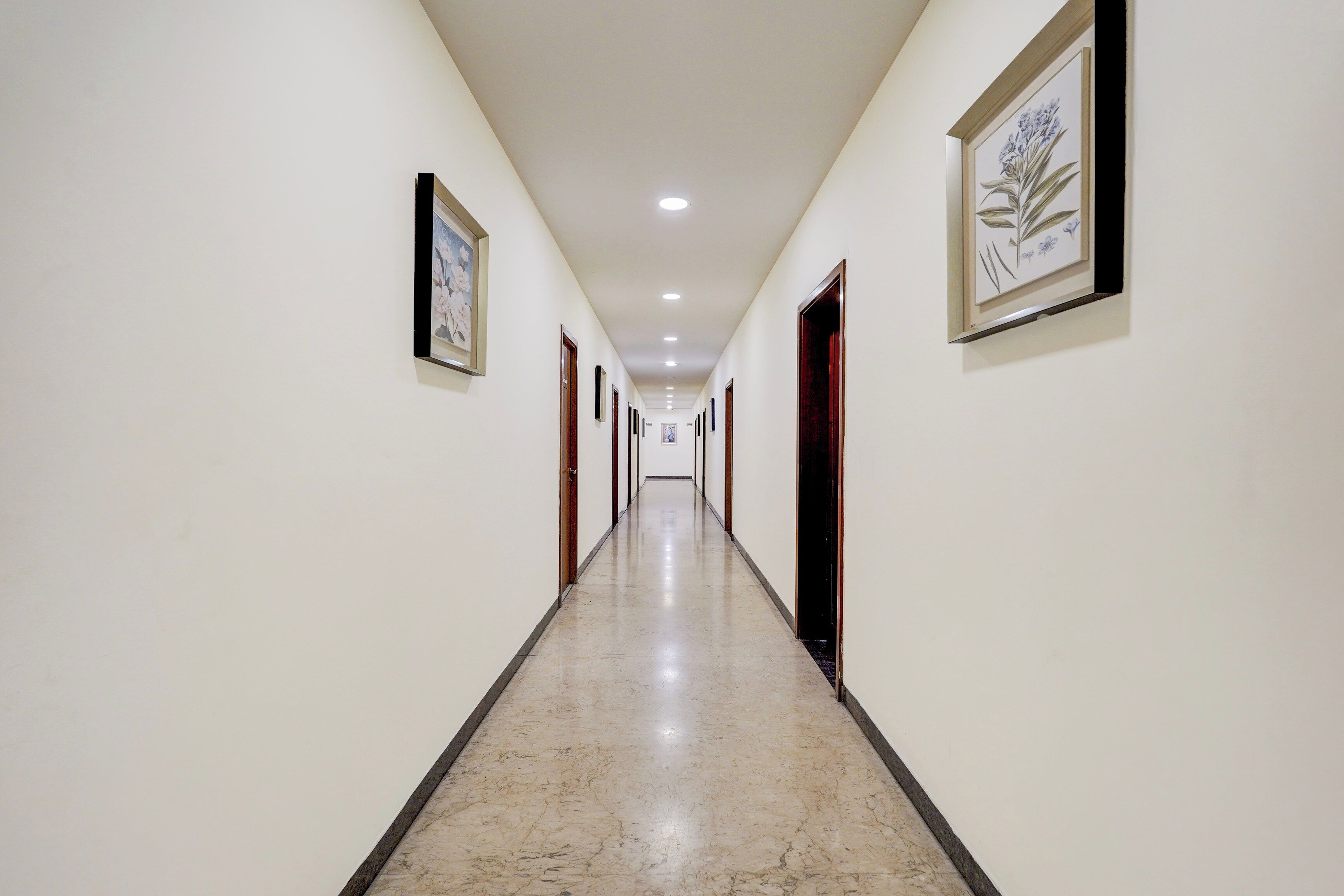A corridor with framed artwork on the walls, doors leading to rooms, and a marble floor.