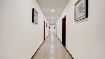 A corridor with framed artwork on the walls, doors leading to rooms, and a marble floor.